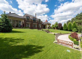 Elegant brick mansion with manicured lawn and garden under a bright blue sky.